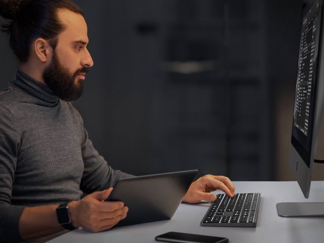 Person using a computer while typing on a Satechi Slim X3 Bluetooth Backlit Keyboard in a dark office.