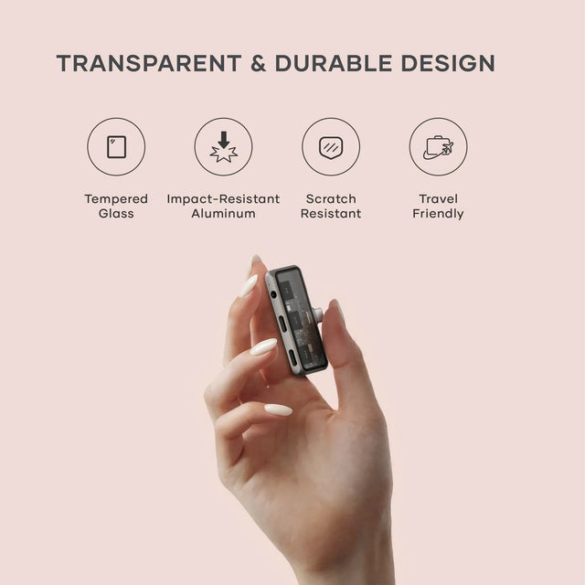 Satechi Mobile XR Hub with Audio held between two fingers, showing its transparent and durable design with icons indicating tempered glass, impact‑resistant aluminum, scratch resistance, and travel‑friendly construction.